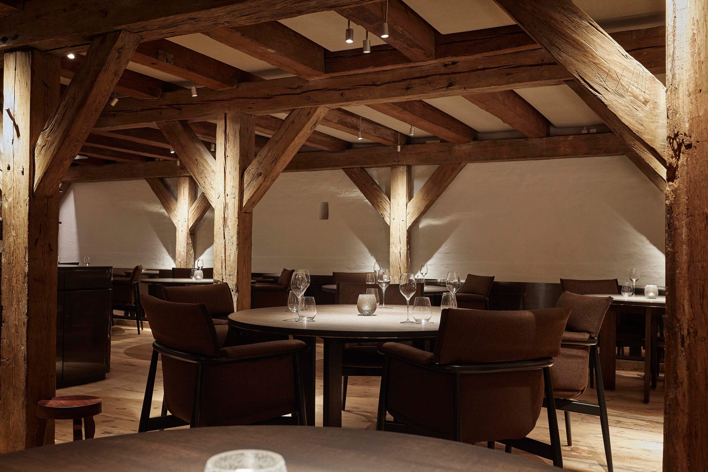 Exposed timber beams above candlelit round tables in Aure’s dining room